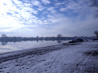 Winter landscape on Sava River . Panoramic scene  with   trees, sun, beautiful frozen river with reflection in water. 