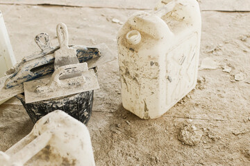 Dirty spatula and trowel with plaster mortar on bucket in unfinished dusty room after repair. Construction of house and home renovation. Professional cleaning up after renovation concept