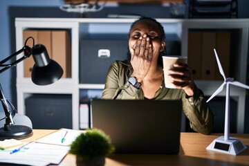 African woman working using computer laptop at night laughing and embarrassed giggle covering mouth with hands, gossip and scandal concept