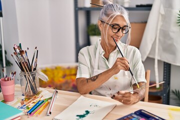Middle age grey-haired woman artist smiling confident drawing on notebook at art studio