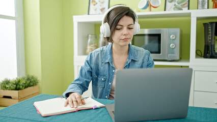 Young caucasian woman using laptop writing on notebook at home