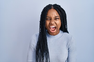 African american woman standing over blue background angry and mad screaming frustrated and...