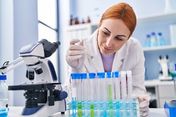 Fototapeta premium Young caucasian woman scientist pouring liquid on test tubes at laboratory