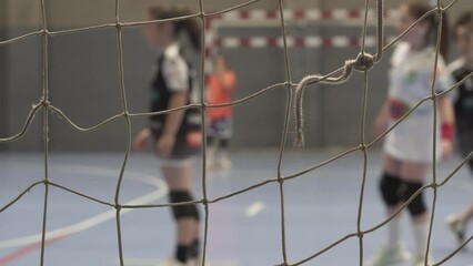 4K footage of girls playing handball and finishing the play in goal in a defocused shot from behind the goal net
