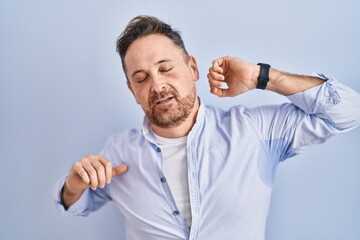 Middle age caucasian man standing over blue background stretching back, tired and relaxed, sleepy and yawning for early morning