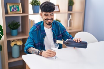 Young hispanic man smiling confident pouring wine on glass at home