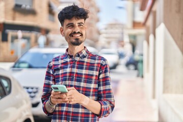 Young hispanic man smiling confident using smartphone at street