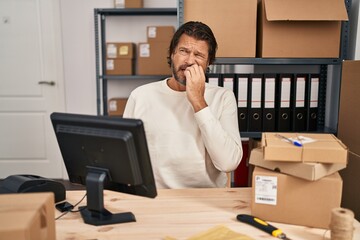 Handsome middle age man working at small business ecommerce looking stressed and nervous with hands on mouth biting nails. anxiety problem.