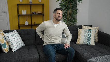 Young hispanic man suffering for backache sitting on sofa at home