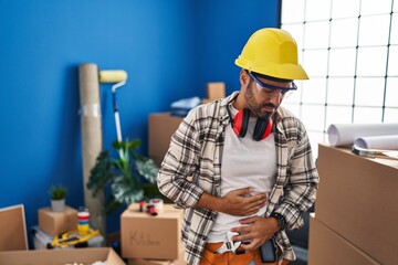 Young hispanic man with beard working at home renovation with hand on stomach because indigestion, painful illness feeling unwell. ache concept.