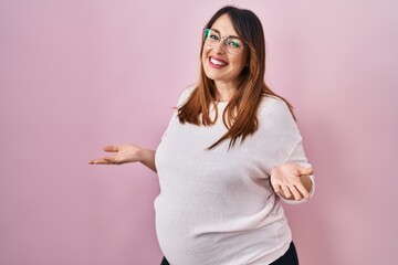 Pregnant woman standing over pink background clueless and confused with open arms, no idea concept.