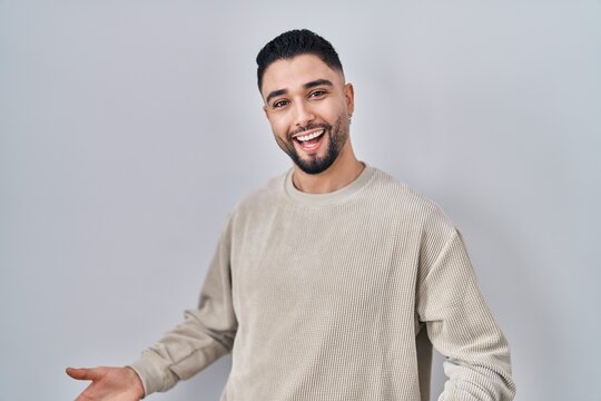 Young handsome man standing over isolated background smiling cheerful with open arms as friendly welcome, positive and confident greetings