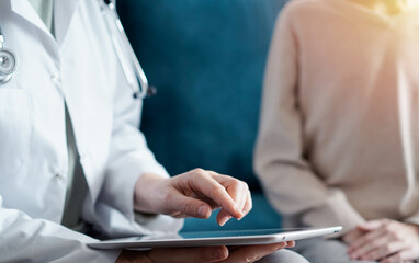 Doctor woman and kid boy patient at home. The pediatrician using tablet computer while filling up medical records, close up. Medicine, healthcare concept.