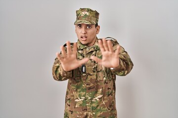 Young arab man wearing camouflage army uniform afraid and terrified with fear expression stop gesture with hands, shouting in shock. panic concept.