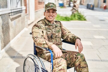 Young arab man wearing camouflage army uniform sitting on wheelchair looking positive and happy...