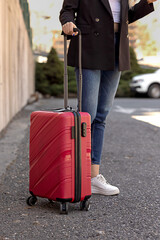 a woman with a red suitcase is waiting on the street, concept of vacation travel or business travel