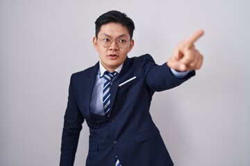 Young asian man wearing business suit and tie pointing with finger surprised ahead, open mouth amazed expression, something on the front