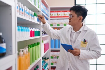 Young chinese man pharmacist using touchpad working at pharmacy
