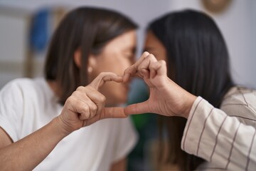 Two women mother and daughter doing heart gesture with hands at bedroom