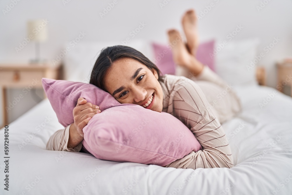 Poster Young hispanic woman hugging pillow lying on bed at bedroom