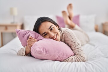 Young hispanic woman hugging pillow lying on bed at bedroom