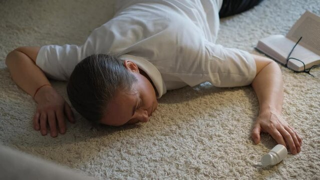 A woman lies unconscious on the floor with scattered pills next to her.