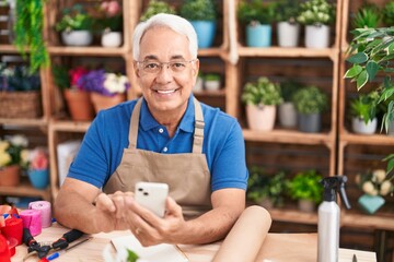 Middle age grey-haired man florist smiling confident using smartphone at florist