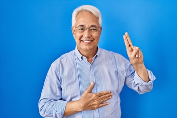Hispanic senior man wearing glasses smiling swearing with hand on chest and fingers up, making a...