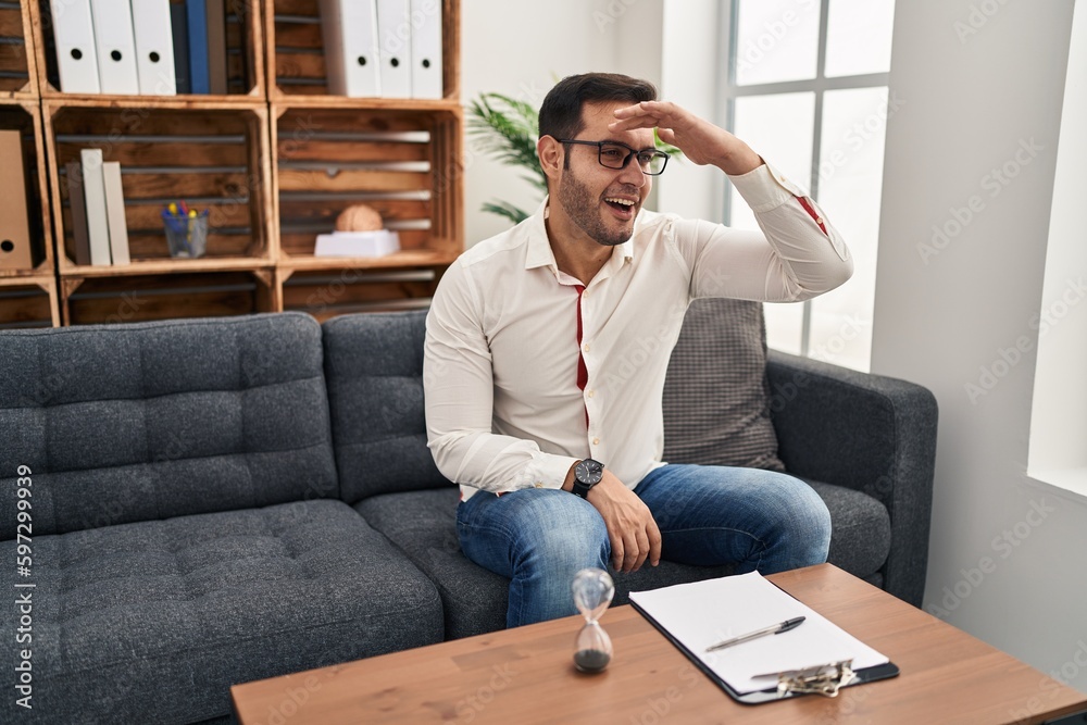 Canvas Prints Young hispanic man with beard working at consultation office very happy and smiling looking far away with hand over head. searching concept.