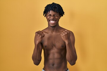 Fototapeta premium Young african man with dreadlocks standing shirtless excited for success with arms raised and eyes closed celebrating victory smiling. winner concept.