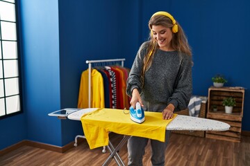 Young blonde woman listening to music ironing clothes at laundry room