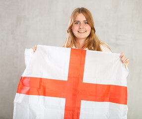 smiling girl holds canvas of English flag in front of her. Gray background.