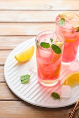Pink cold lemonade from hibiscus tea with lemon slices and ice cubes in glasses on a wooden background. Refreshing soft drinks.