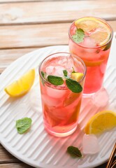 Pink cold lemonade from hibiscus tea with lemon slices and ice cubes in glasses on a wooden background. Refreshing soft drinks.