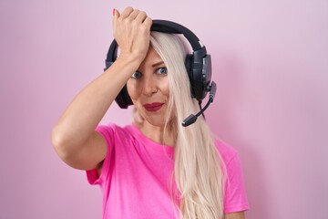 Caucasian woman listening to music using headphones surprised with hand on head for mistake,...