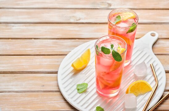 Pink cold lemonade from hibiscus tea with lemon slices and ice cubes in glasses on a wooden background. Refreshing soft drinks.