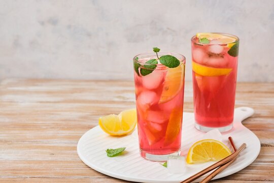 Pink cold lemonade from hibiscus tea with lemon slices and ice cubes in glasses on a wooden background. Refreshing soft drinks.