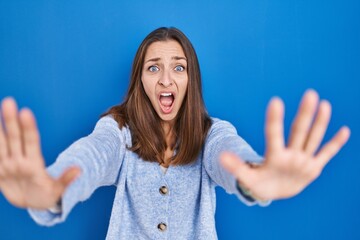 Young woman standing over blue background doing stop gesture with hands palms, angry and frustration expression