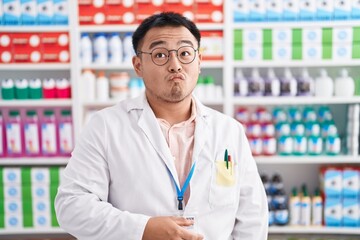 Chinese young man working at pharmacy drugstore making fish face with lips, crazy and comical gesture. funny expression.