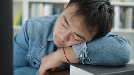 Young chinese man student sleeping on books at library university