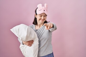Woman with down syndrome wearing sleeping mask hugging pillow gesturing finger crossed smiling with hope and eyes closed. luck and superstitious concept.