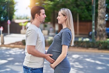 Man and woman couple standing together touching belly at street