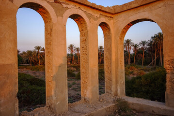 Arab historical building consisting of columns and windows made of clay and rocks, overlooking a nature of palm trees and green trees
