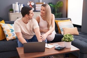 Man and woman couple expecting baby using laptop accounting at home