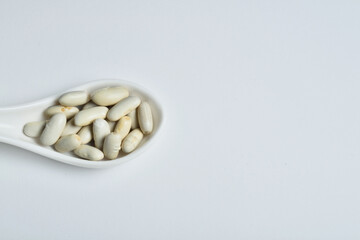 Fototapeta na wymiar White ceramic spoon full of beans on white background.