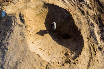 Top view of a man standing in a sandy hole that looks like a lunar crater
