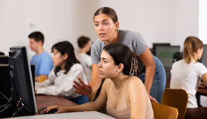 Fototapeta premium Schoolgirl using computer and teacher helping to him in classroom
