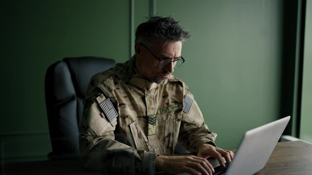 Soldier with glasses working with laptop in home. Everyday life of a military man in reserve. Work and communication online