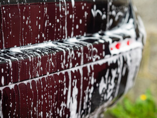 Dirty water with foam on a dark metal surface of a car. Cleaning and valeting of a vehicle concept.
