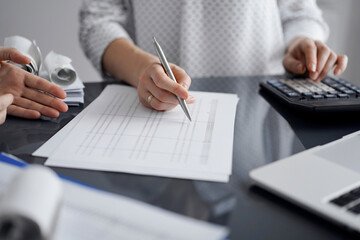 Woman accountant using a calculator and laptop computer while counting and discussing taxes with a client. Business audit and finance concepts